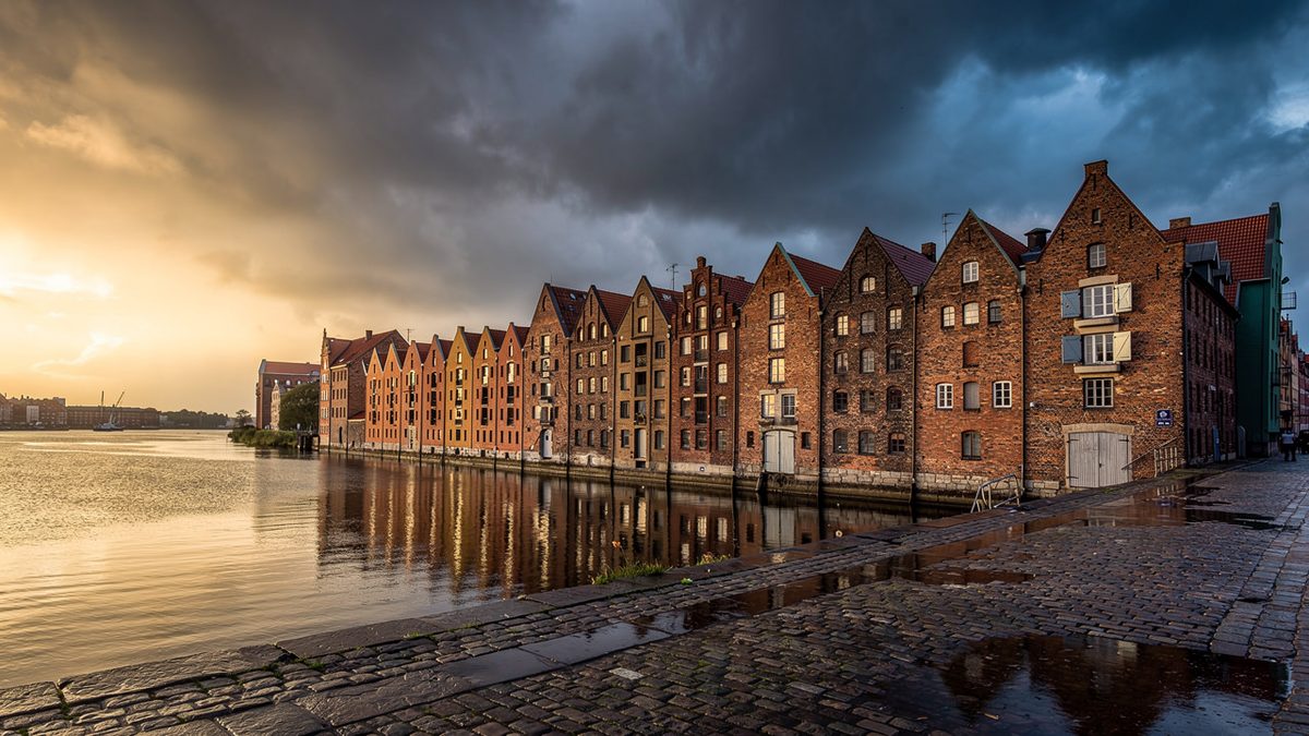 Brick granaries on a Baltic riverside under half-sunny, half-rainy skies (illustration)