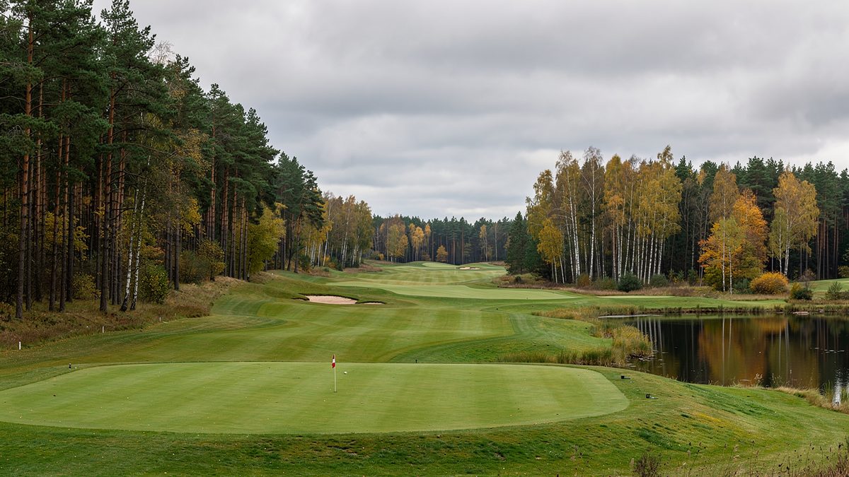 A golf fairway lined with pine and birch forest beside a small lake, typical of courses in the Pomeranian countryside (illustration)